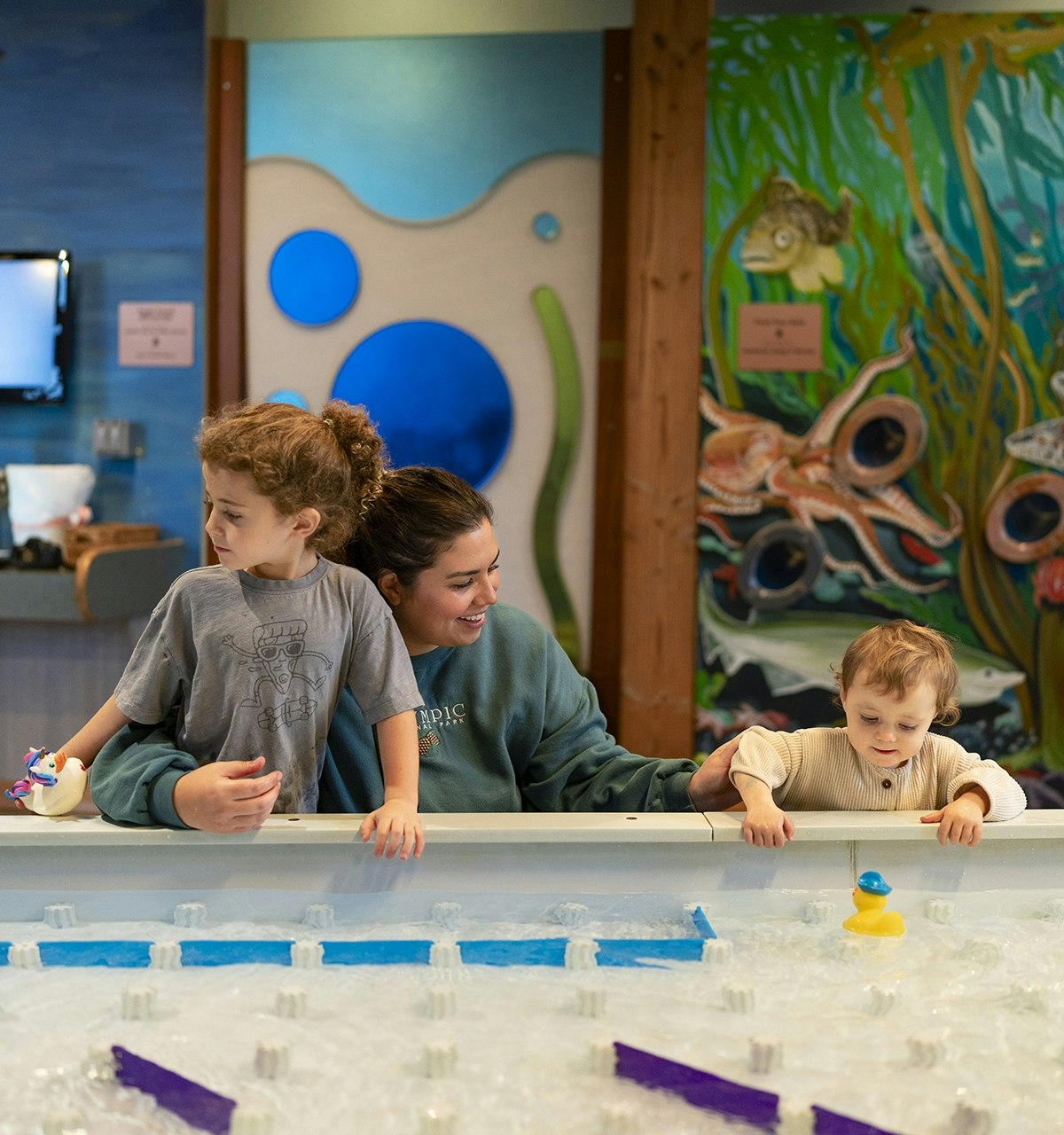 A woman enjoys sharing interactive experiences with two children at a science center.
