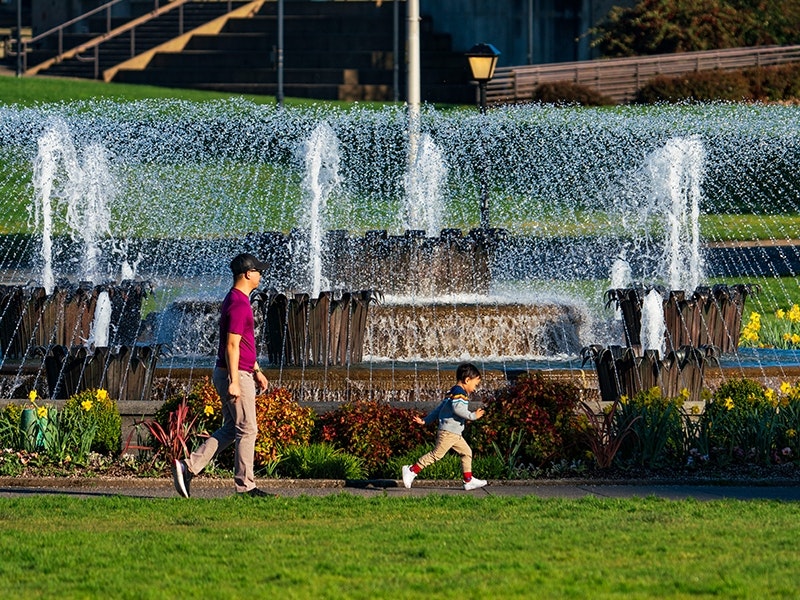 A father and child running past a water fountain.