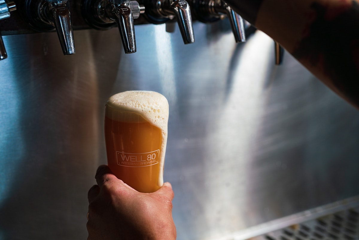Foam cascades down the side of a full glass of beer beneath taps at Well 80 Brewhouse in Olympia, WA